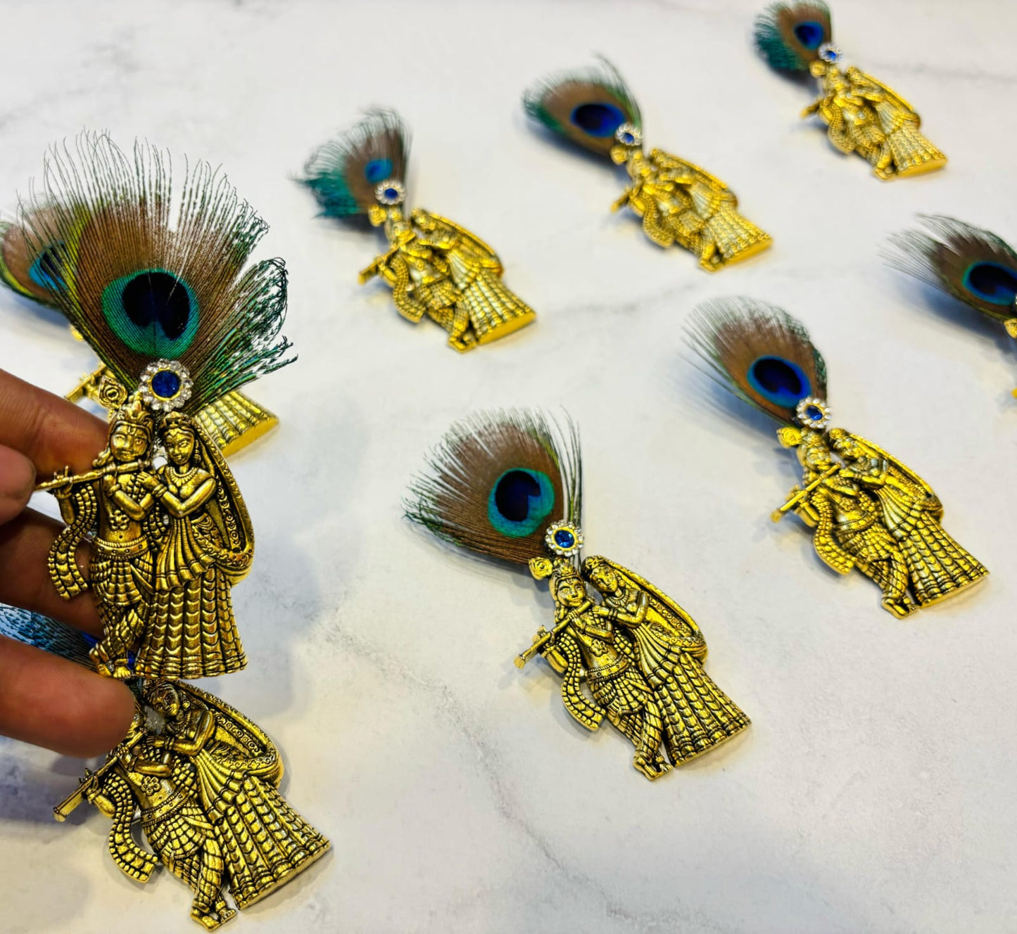 Matte gold Radha Krishna brooch featuring a peacock feather and a blue stone accent.